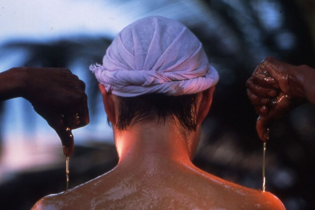 A person receiving Pizhichil therapy, with warm medicated oil being poured continuously over their body for nourishment and detoxification