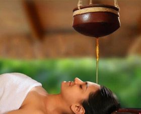 A person receiving Shirodhara therapy, with warm herbal oil gently flowing onto their forehead, promoting relaxation and mental clarity.