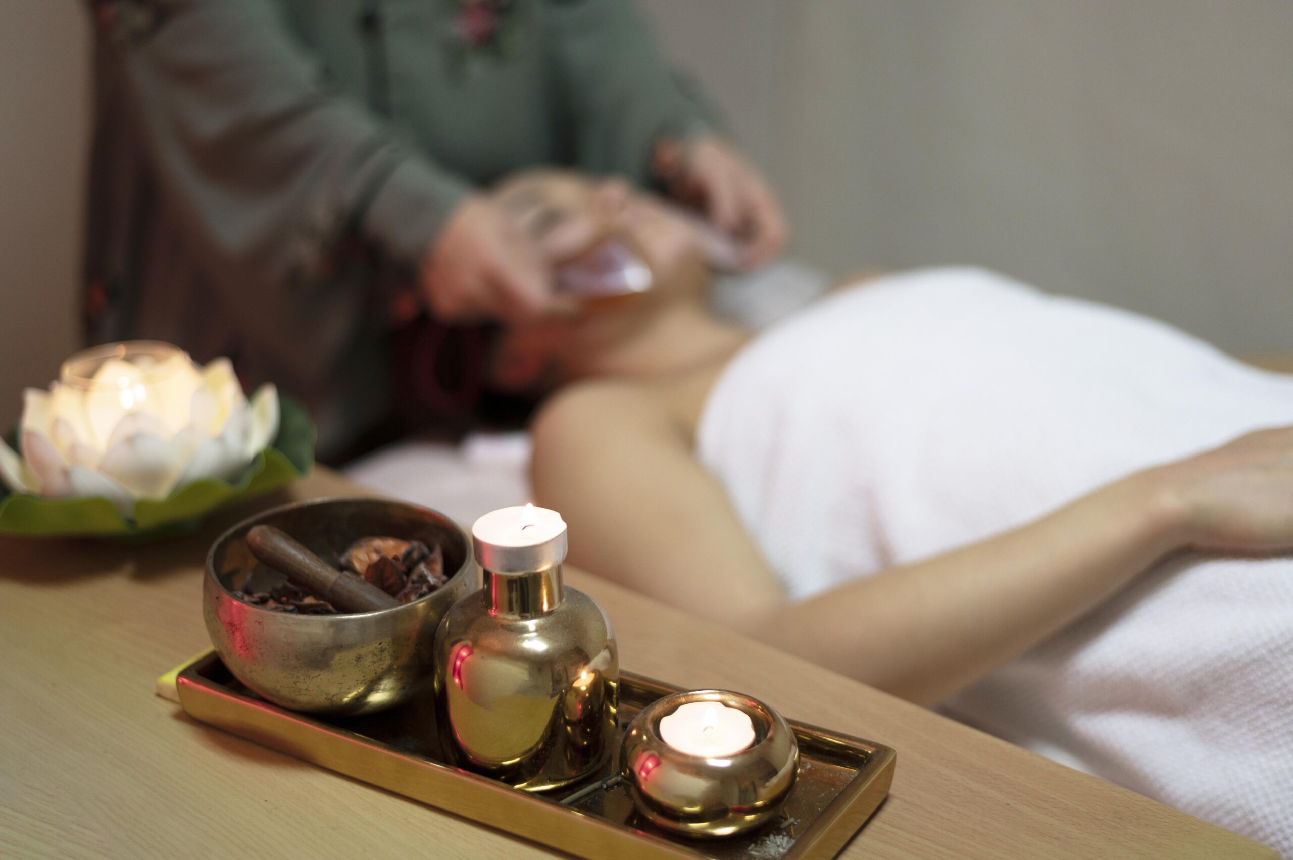 A woman receiving a facial massage in a relaxing spa setting with candles, essential oils, and decorative items in the foreground.